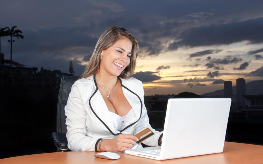 woman in business attire is smiling while watching something on her laptop