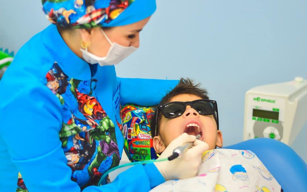 dentist checking the moth of the little boy who is wearing a black sunglasses